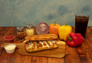 Genos Giant Slice pizza on wooden board with fresh vegetables and condiments beside it