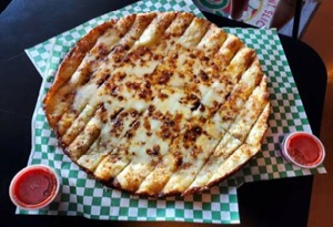 Genos Giant Slice pizza on checkered paper with two small sauce cups nearby