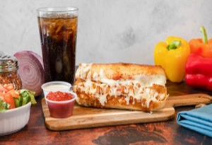 Genos Giant Slice pizza on wooden board with sides, drink, and fresh vegetables on rustic table