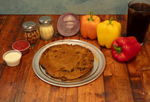 Genos Giant Slice pizza on metal plate with fresh peppers, onions, and condiments on wooden table