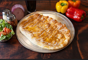 Genos Giant Slice pizza on metal tray with fresh vegetables and condiments on wooden table