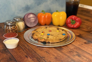 Genos Giant Slice pizza on metal plate with colorful peppers and condiments on wooden table