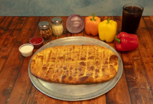 Genos Giant Slice pizza on metal tray with pepperoni, cheese, and sauce toppings, served with peppers and soda on wooden table