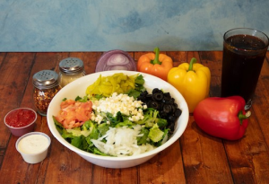 Genos Giant Slice pizza in white bowl with toppings, surrounded by vegetables and condiments on wooden table