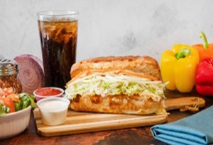 Genos Giant Slice sandwich on wooden board with side dishes and soda drink
