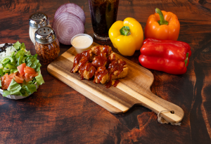 Genos Giant Slice pizza with barbecue chicken, vegetables, and sides on wooden board
