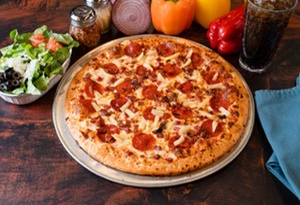 image010 Genos Giant Slice pizza with pepperoni, cheese, and toppings on a metal tray, surrounded by vegetables and a drink.