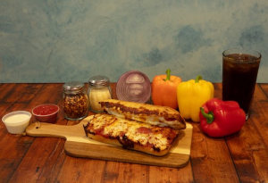 Genos Giant Slice pizza on wooden board with peppers, condiments, and drink on rustic table