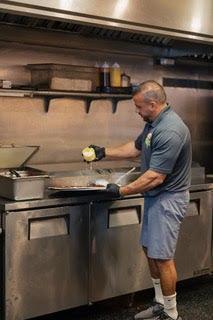 Genos Giant Slice pizzeria kitchen staff preparing pizza on stainless steel counter with visible signage and equipment