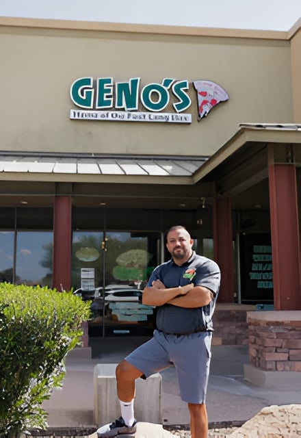 Man standing outside Geno's Giant Slice pizzeria with arms crossed, storefront sign visible above entrance