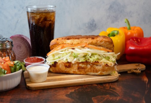 Genos Giant Slice sandwich on wooden board with sides, drink, and condiments visible
